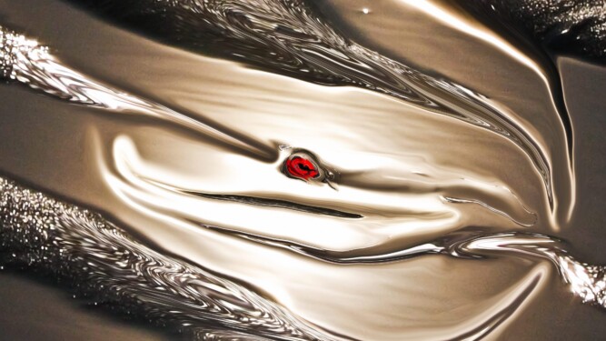 Sunlight reflections on smooth water and sand, in fluid brown color with a silky texture. Abstract photo with reflections of light in dominant gold color with a red symbol in the center.